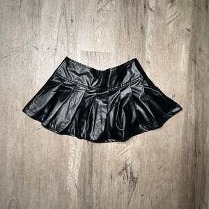 Black faux leather pleated mini skirt with zipper and button closure. Size: S
